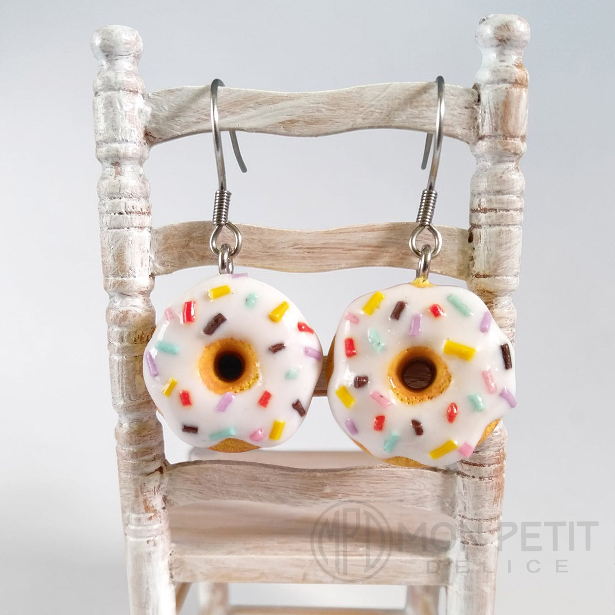 Polymer clay white donut earrings displayed on a rustic miniature wooden chair.