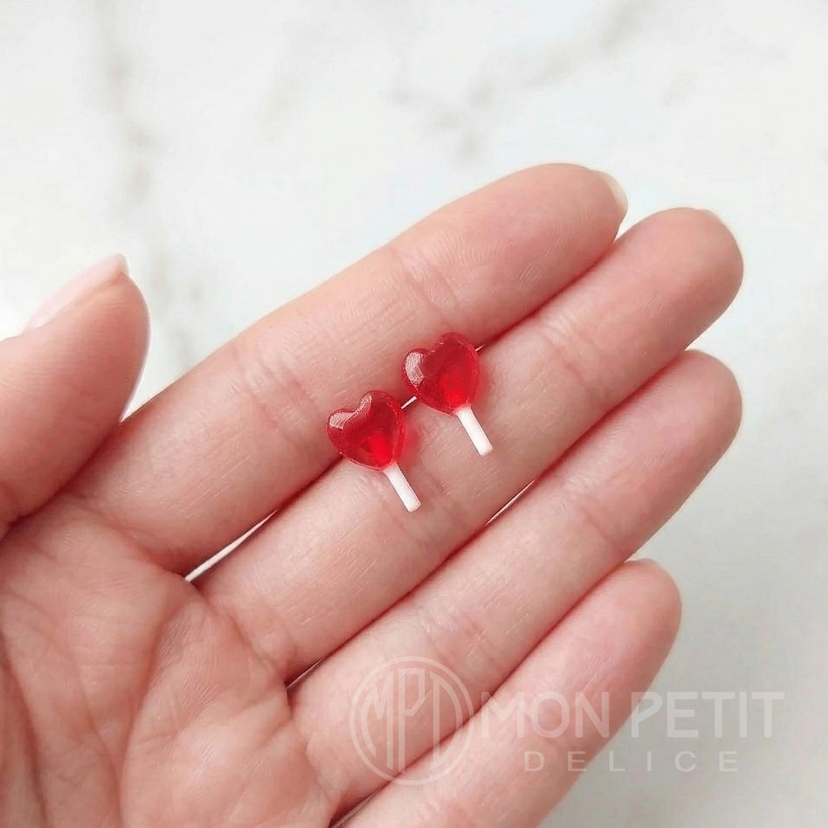 Handmade red heart lollipop earrings shown on fingers to display size