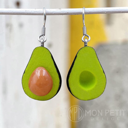 Cute avocado earrings hanging on a white wire, showing one half with pit and one half without. Perfect foodie gift.