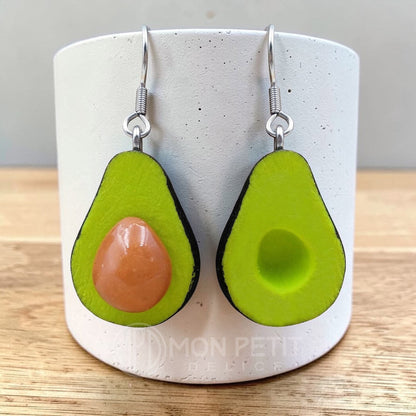 Handmade avocado earrings in polymer clay displayed against a modern white ceramic stand.