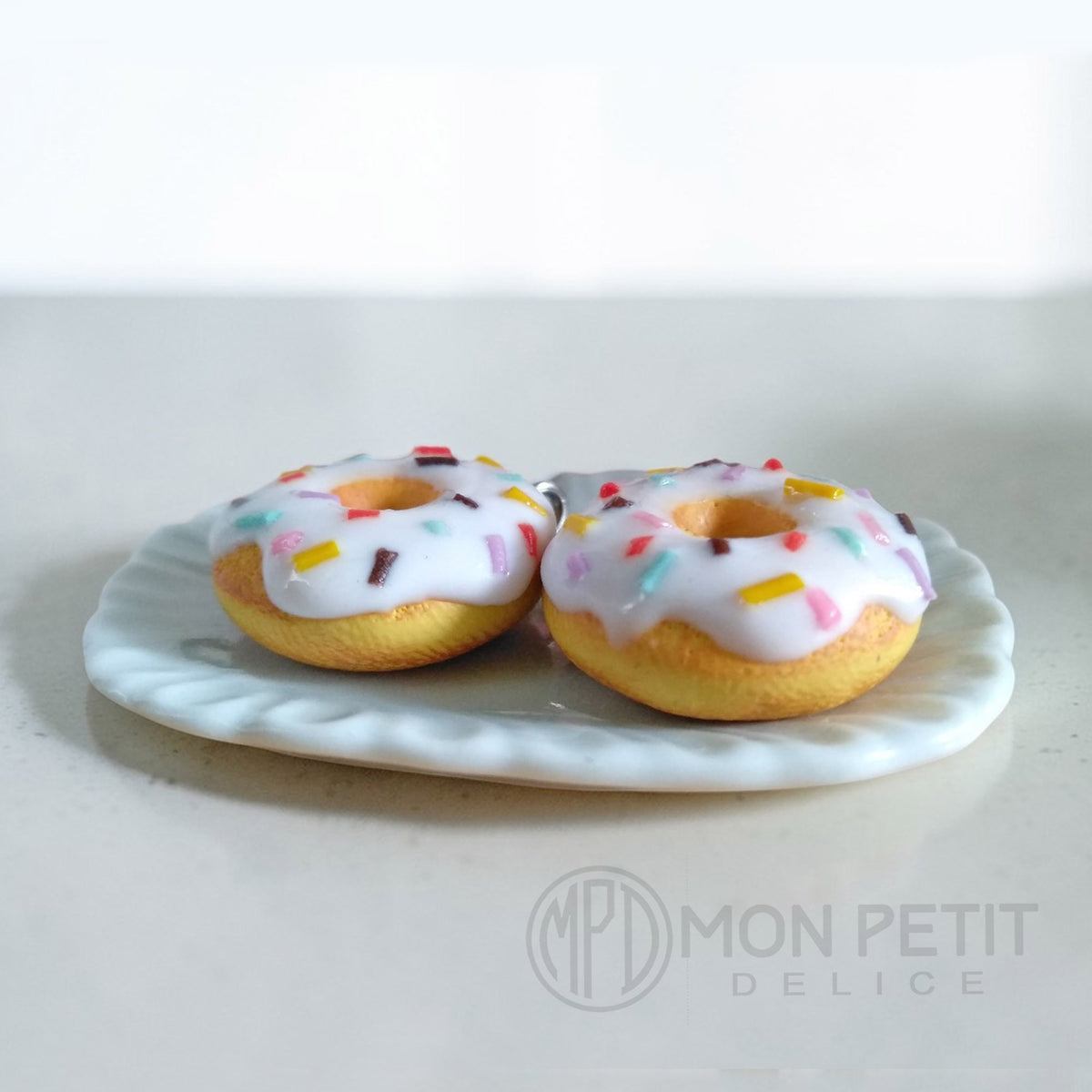 Macro close-up of the glossy white icing and rainbow sprinkles on foodie jewelry.