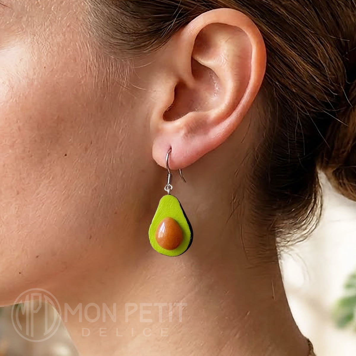 Lightweight avocado dangle earrings worn on ear for size reference.