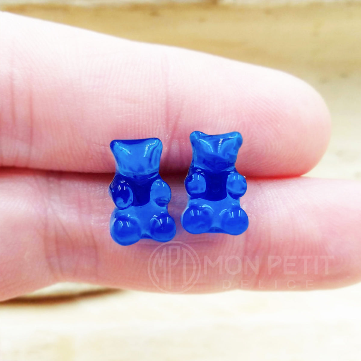Blue gummy bear stud earrings shown on fingers for size reference